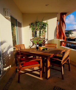 Ein Holzespeisetisch mit Stühlen, einem Blumentopf und einer Weinflasche auf einem Balkon mit Meerblick.