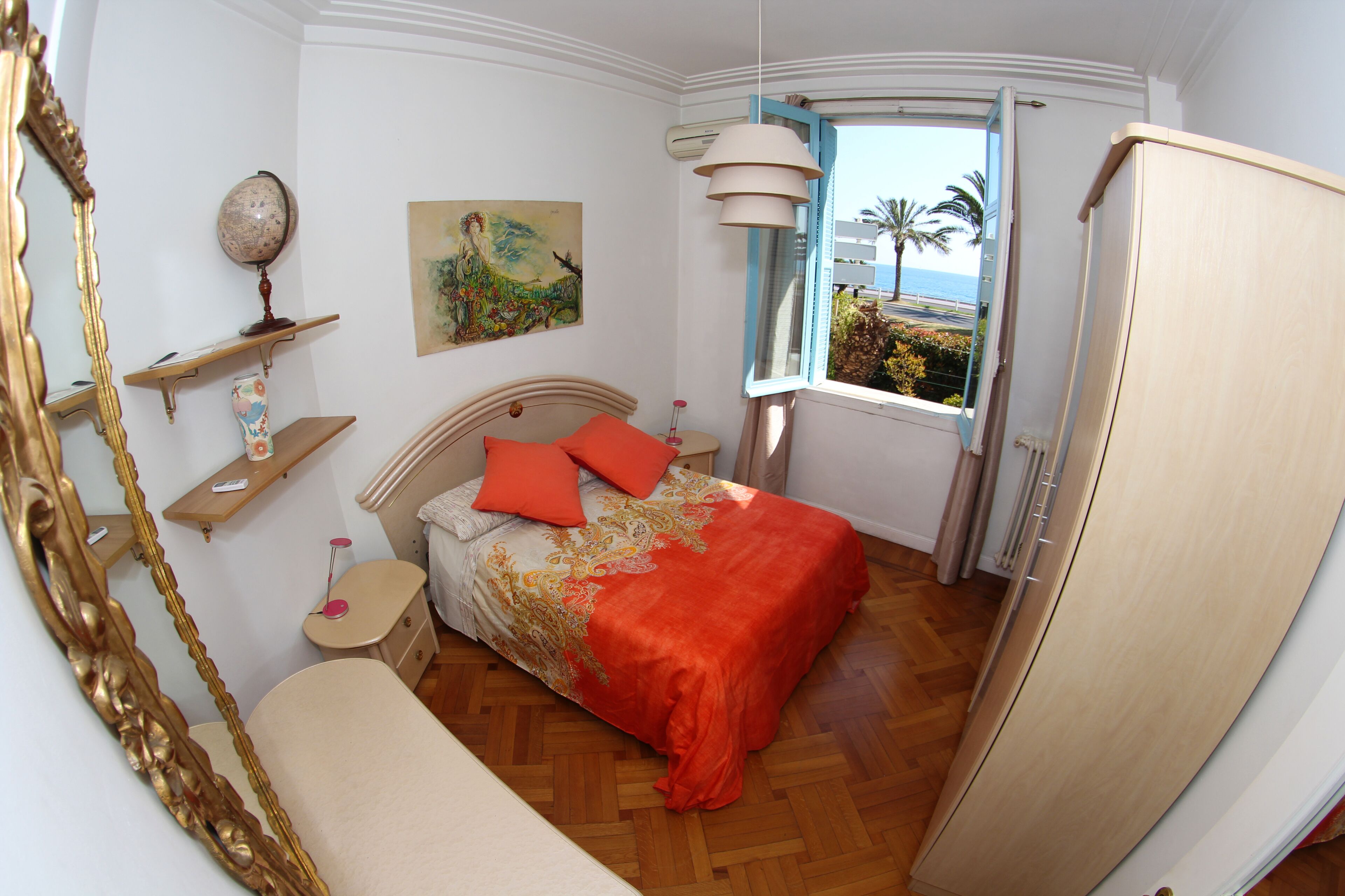 A bedroom with a bed, a bedside table, a dresser, a window with a view, and a mirror.