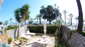 Une terrasse extérieure avec une table dressée pour le dîner, entourée de plantes en pot et de palmiers, donnant sur une plage.