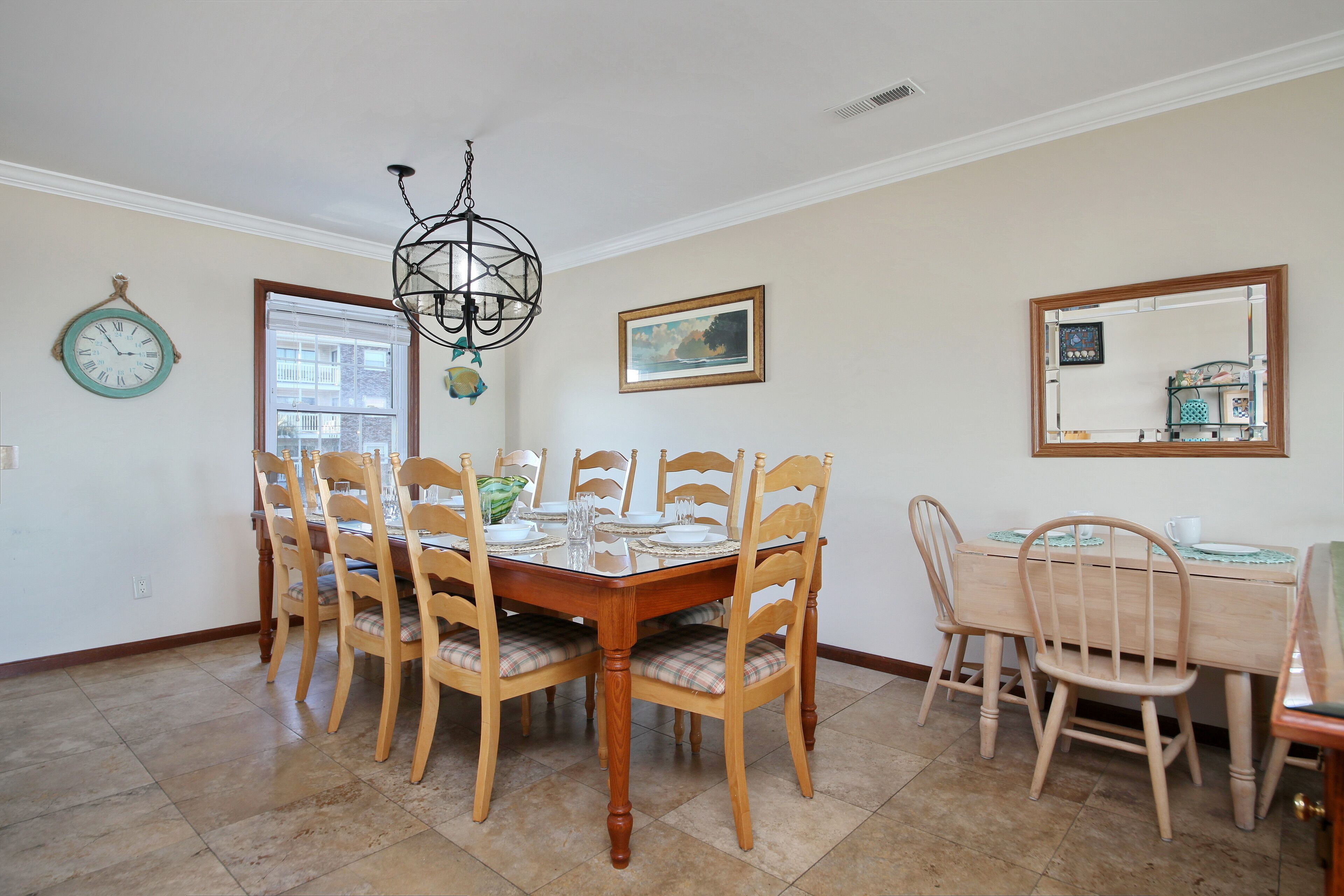 Uma sala de jantar com uma mesa e cadeiras de madeira, um candelabro, um relógio e um quadro na parede.