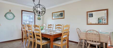 Uma sala de jantar com uma mesa e cadeiras de madeira, um candelabro, um relógio e um quadro na parede.