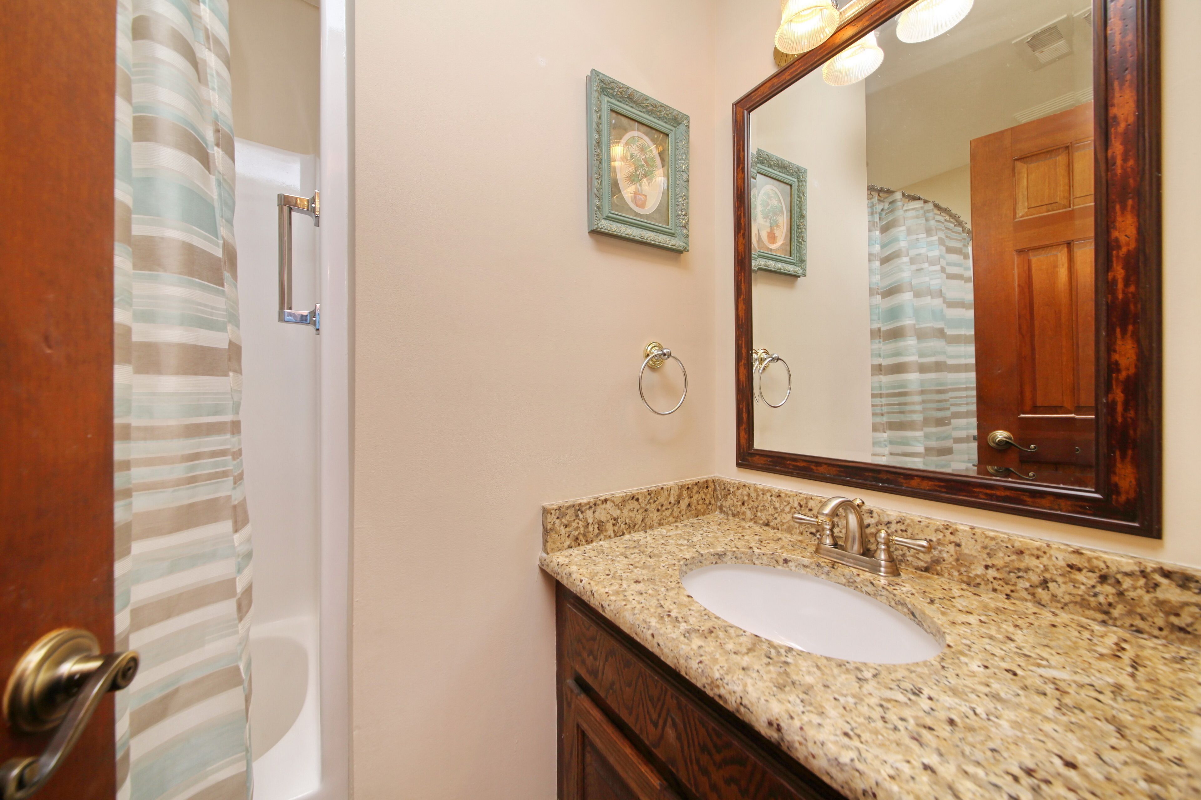 A bathroom with a granite countertop sink, a wooden vanity, a large mirror, and a shower curtain.