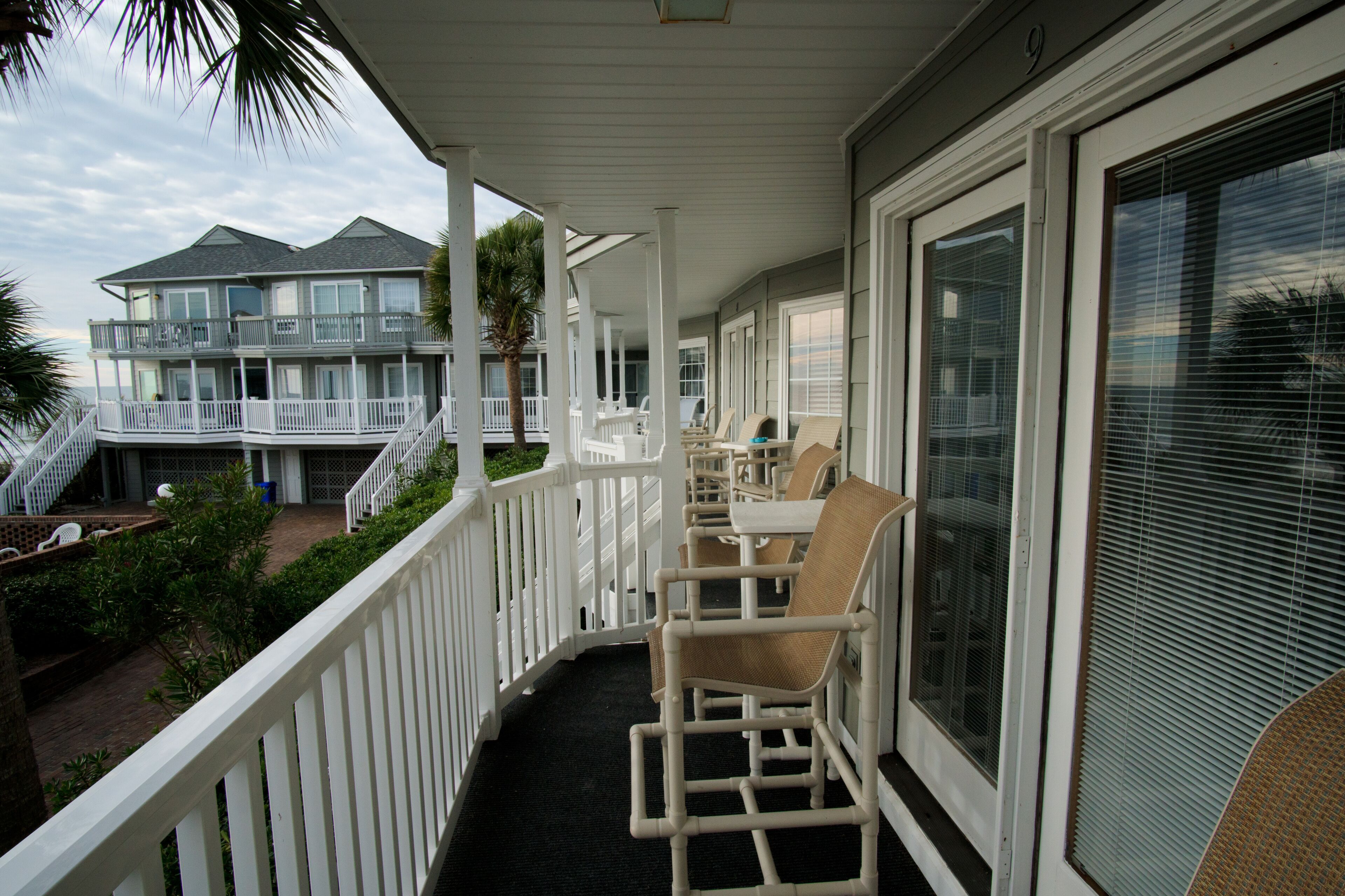 A balcony with white railings, wicker chairs, and a view of a building with multiple balconies.
