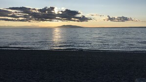Een strand met een heldere lucht, rustige zee en land in de verte.