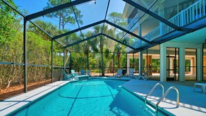 Une piscine à l’eau d’un bleu cristallin, entourée d’un espace abrité avec des chaises longues, d’où l’on peut admirer des arbres et un bâtiment en arrière-plan.