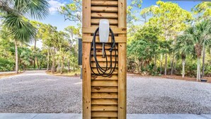 Une structure en bois, avec un objet blanc et des câbles, entourée d’une zone de gravier et de palmiers.