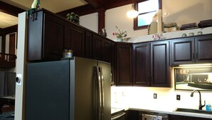 A kitchen with dark wooden cabinets, a stainless steel refrigerator, and a window above the sink. - Knights of Pythias Loft Downtown Albany, Oregon 2400 Sq Ft Of Space (ALBANY)