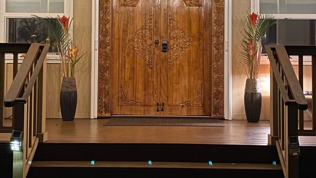 A grand wooden double door with intricate carvings, flanked by two potted plants, leading to a staircase with wooden railings. - *Peace and Serenity* (Haiku)