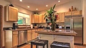 A modern kitchen with wooden cabinets, a stainless steel refrigerator, and a central island with stools. - *Peace and Serenity* (Haiku)