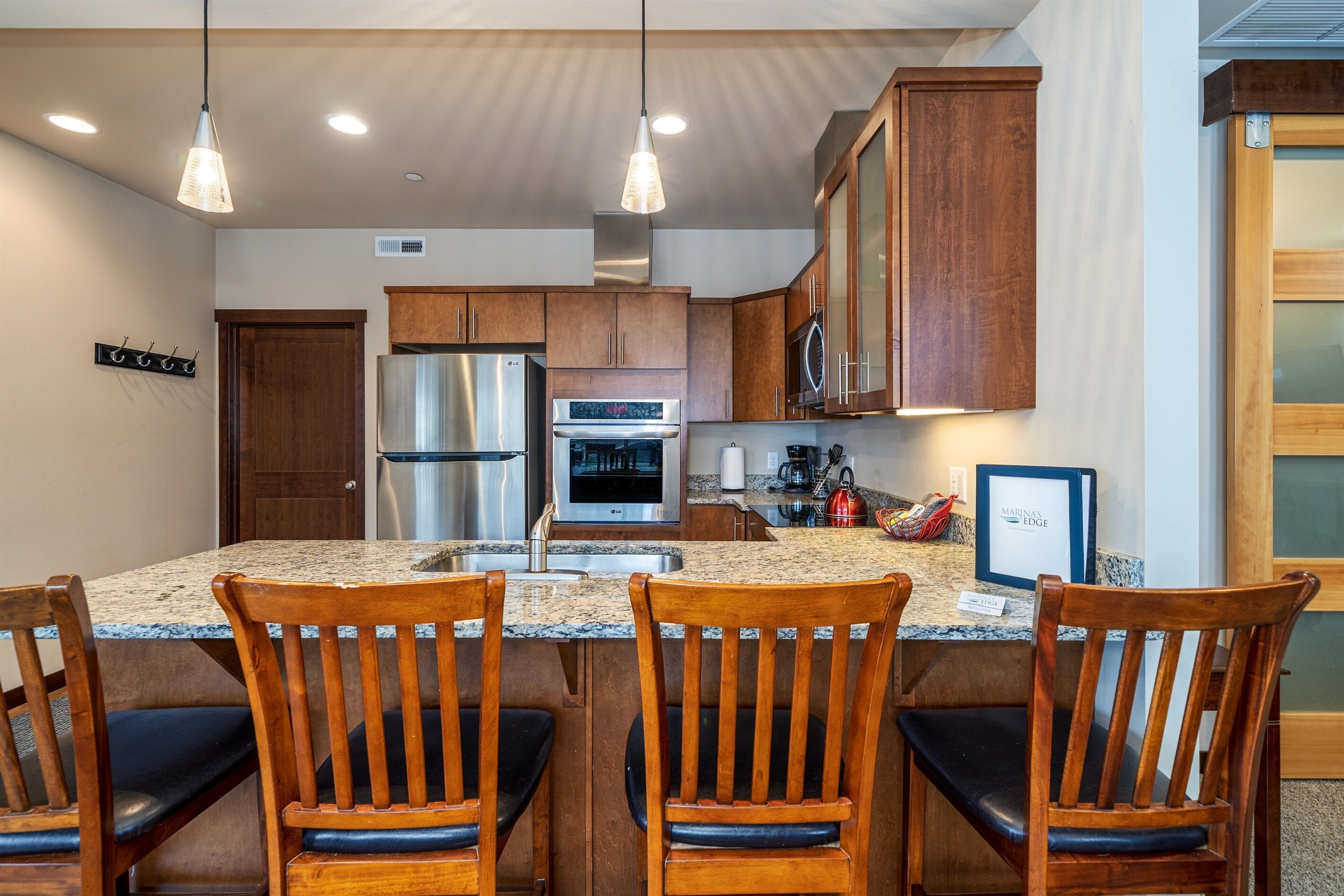 A modern kitchen with granite countertops, stainless steel appliances, wooden cabinets, and a central island with bar seating.