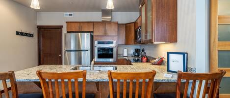A modern kitchen with granite countertops, stainless steel appliances, wooden cabinets, and a central island with bar seating.