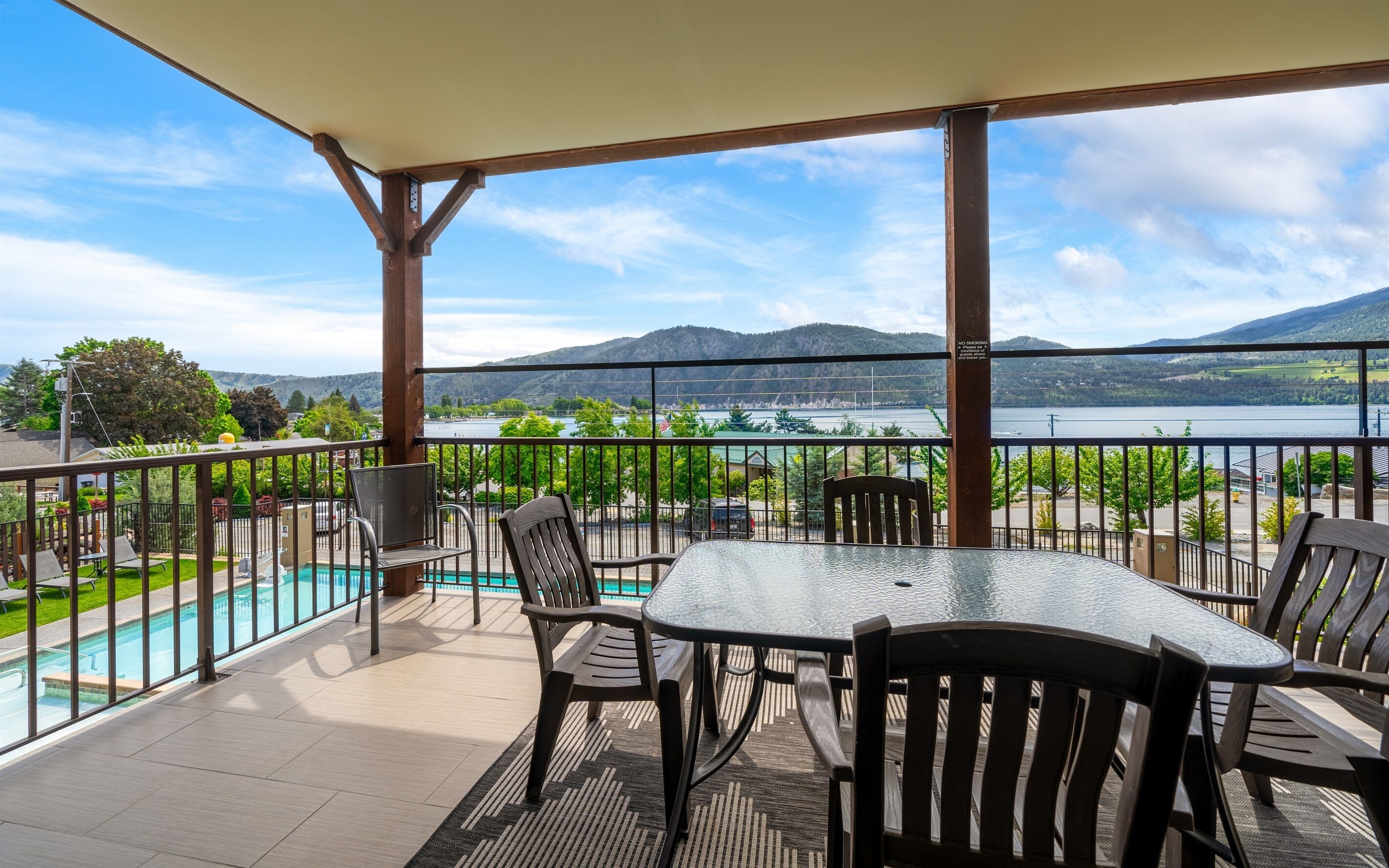 A balcony with a table and chairs, overlooking a lake and mountains.