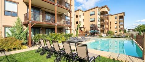 A pool area with lounge chairs, a wooden deck, and a building with balconies.