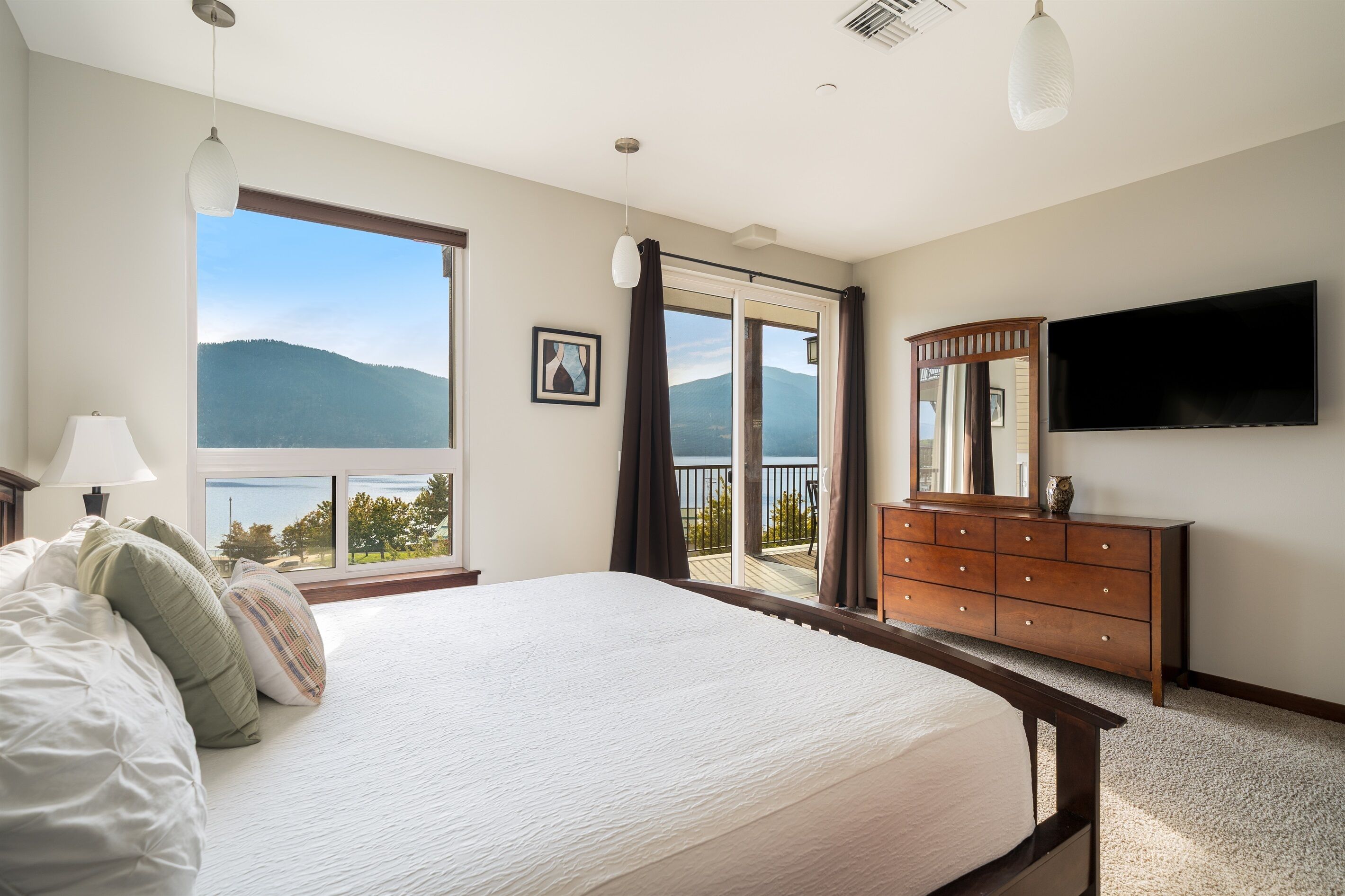 A bedroom with a large bed, a dresser, a TV, and a view of mountains through a sliding door.