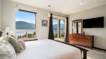 A bedroom with a large bed, a dresser, a TV, and a view of mountains through a sliding door.