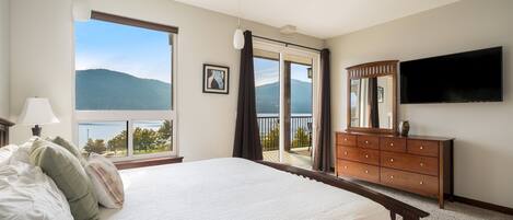 A bedroom with a large bed, a dresser, a TV, and a view of mountains through a sliding door.