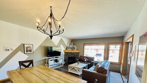 A living room with a wooden dining table, a sofa, a TV, and a fireplace.