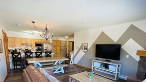 A spacious living area with a brown leather sofa, wooden tables, and a kitchen in the background.