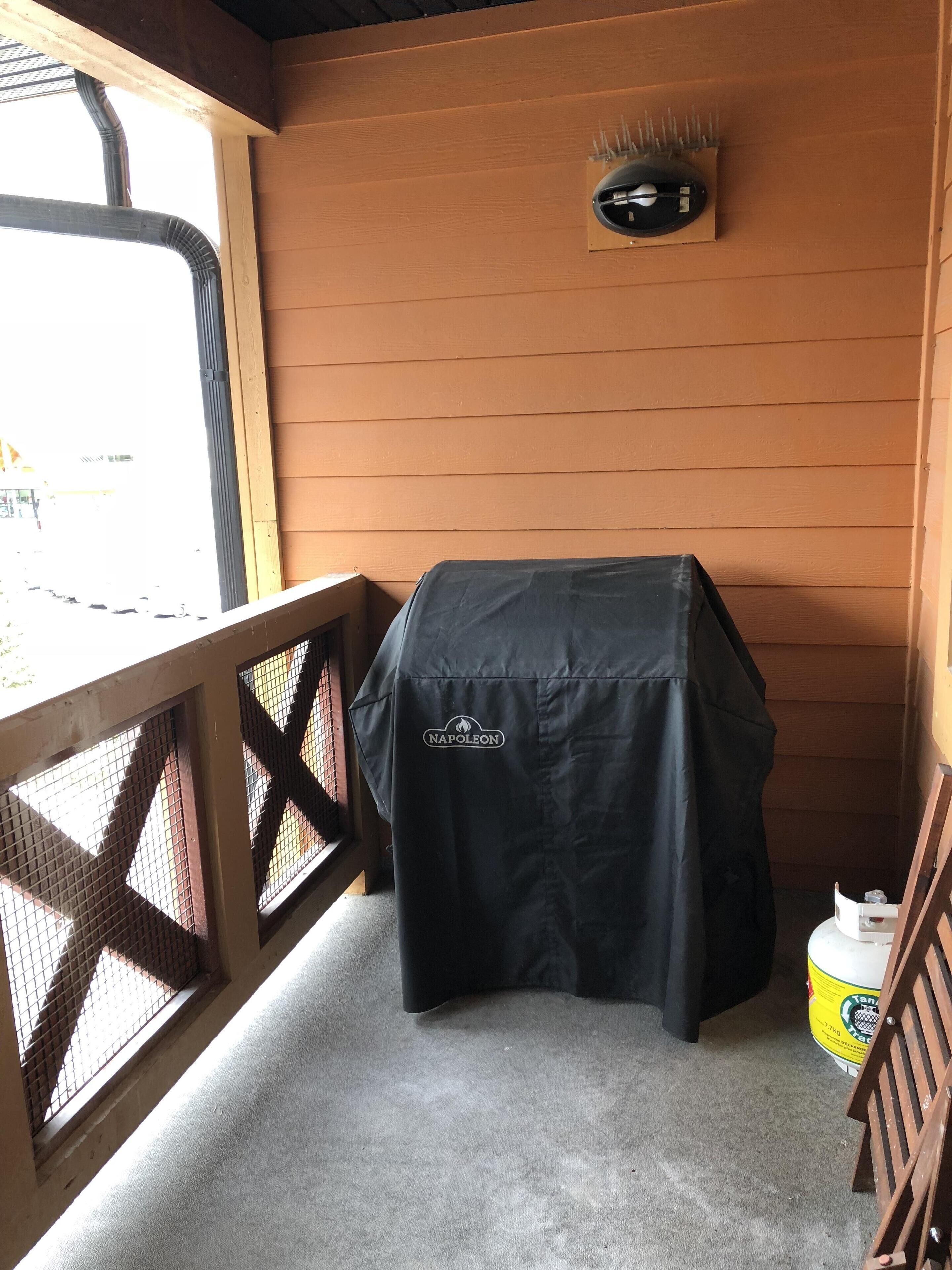 Ein überdachter Außenbereich mit Tisch, Grill und einem großen, gelben Behälter.