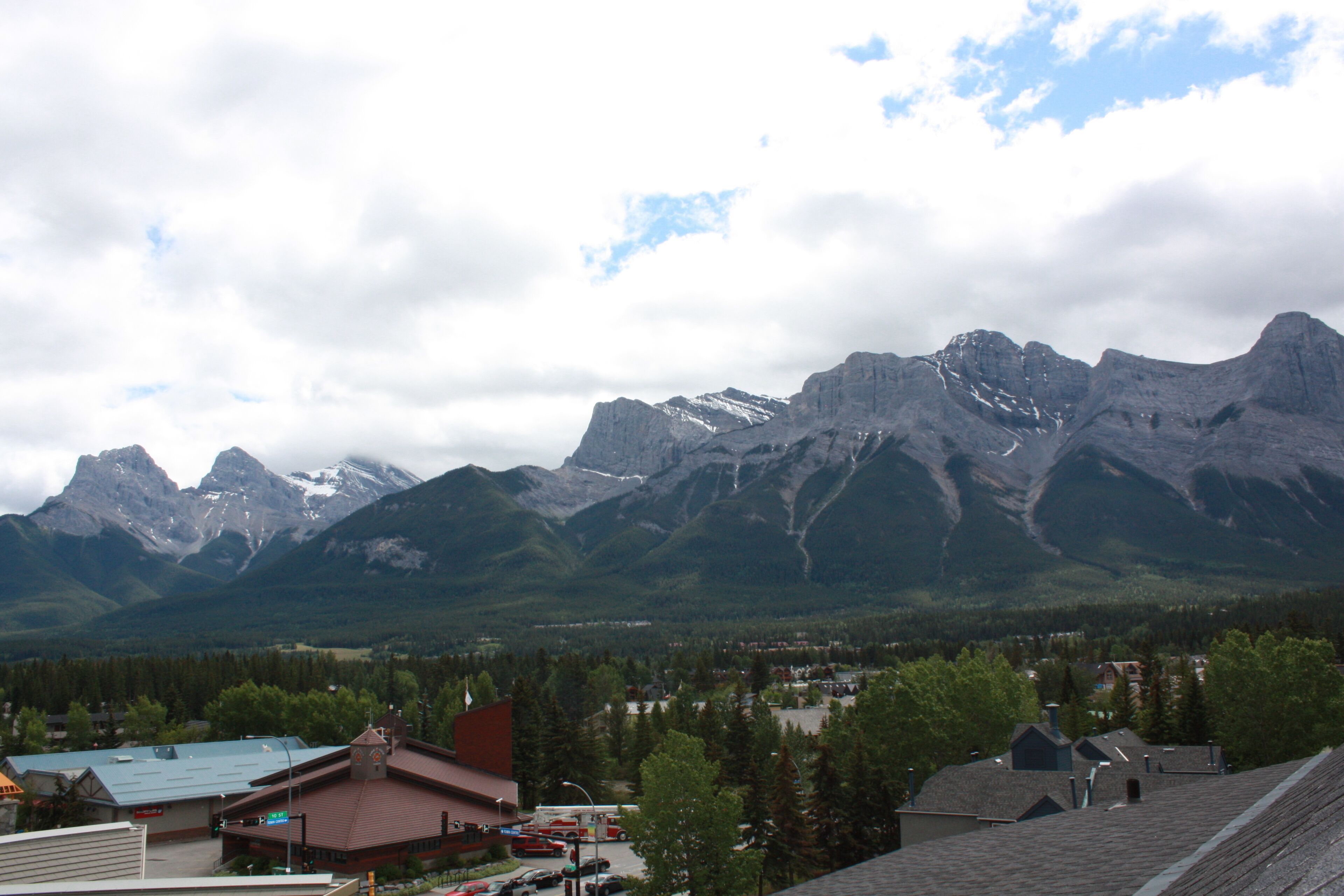 A mountain town with a prominent mountain range in the background, a mix of residential and commercial buildings, and a clear sky.