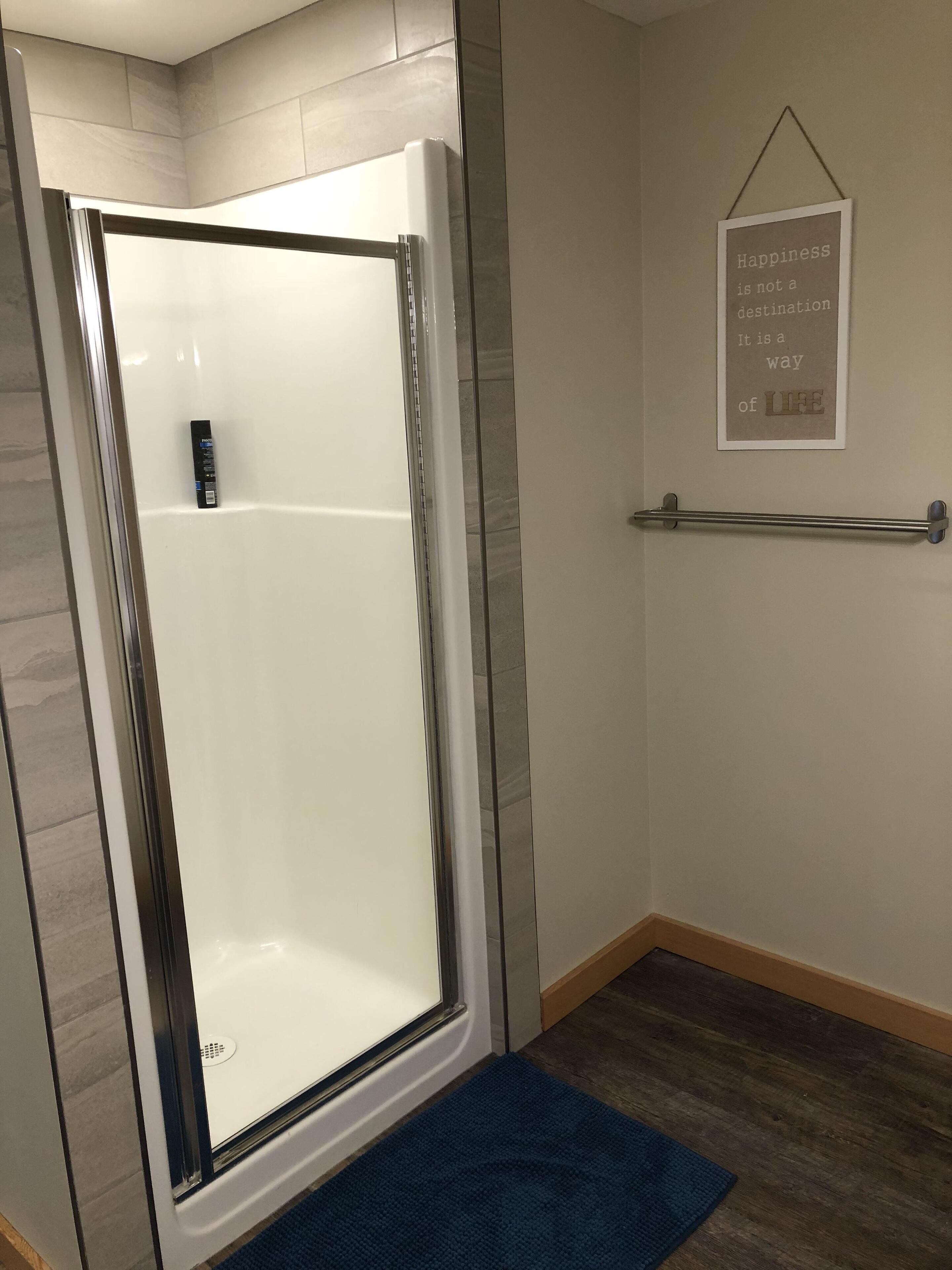 A modern bathroom with a glass shower enclosure, a towel rack, and a motivational quote on the wall.