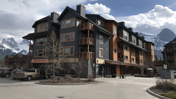 A multi-story hotel with balconies, a sign for a liquor depot, and a view of snow-capped mountains in the background.