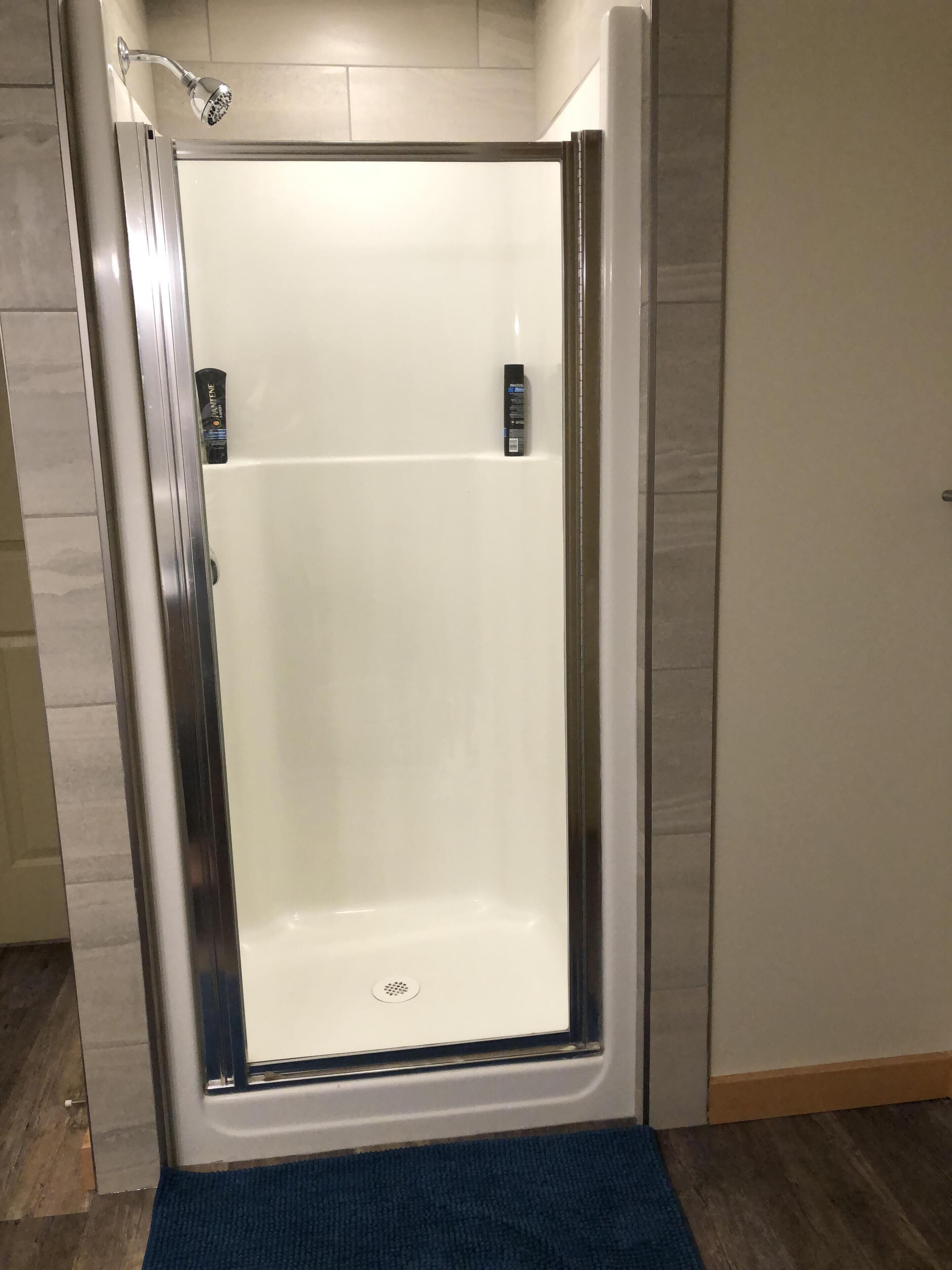 A walk-in shower with a glass door, a handheld showerhead, and a handheld body wash dispenser.