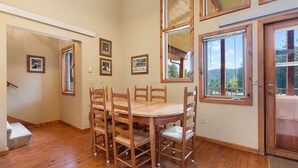 A dining area with a wooden table and chairs, framed pictures on the wall, and large windows with a view of trees. - Large private lot.  Beautiful cabin with a stream and trout pond!  (Lead)