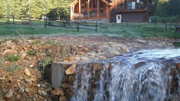 A wooden cabin with a porch and a small waterfall in front. - Large private lot.  Beautiful cabin with a stream and trout pond!  (Lead)