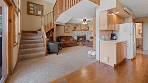 A spacious living area with a fireplace, a kitchen with wooden cabinets, and a staircase leading to an upper level. - Large private lot.  Beautiful cabin with a stream and trout pond!  (Lead)