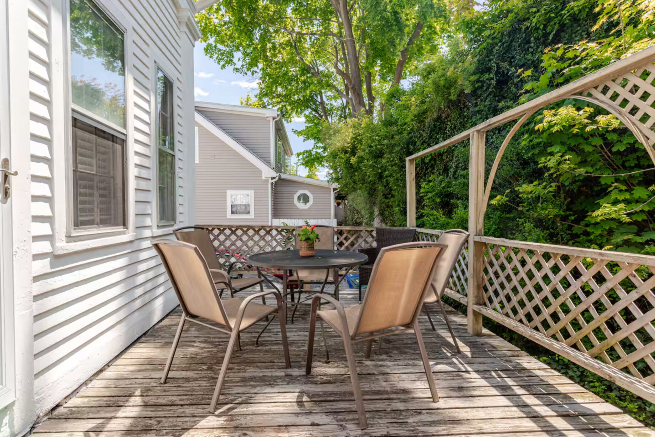 A wooden deck with a round table and four chairs, surrounded by a wooden lattice fence.