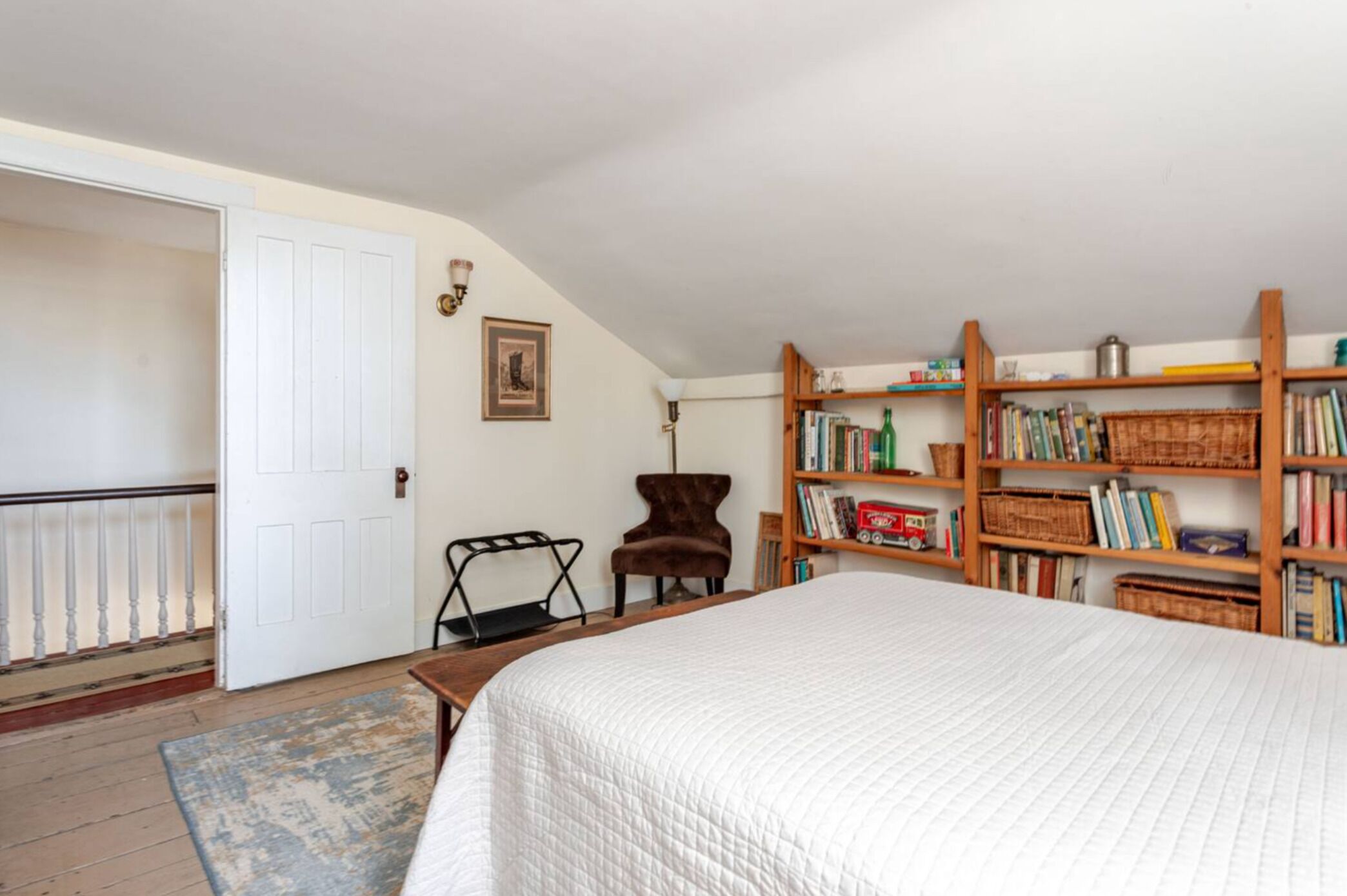 A bedroom with a large bed, a wooden bookshelf, a chair, and a door.