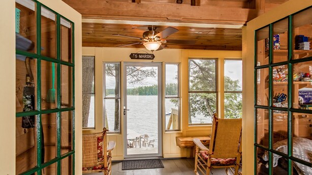 L’intérieur chaleureux d’un chalet, avec une grande fenêtre donnant sur un lac, un ventilateur de plafond et une pancarte indiquant « 5 Marsh ».