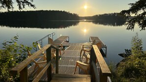 Une jetée en bois, agrémentée de chaises et d’une table, qui mène à un lac paisible entouré d’arbres.