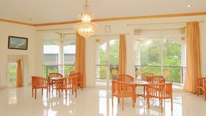 A spacious room with a large dining table and chairs, large windows with curtains, and a chandelier. - OYO Life 414 Loji Rejo Guest House (Malang)