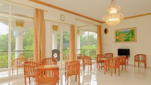 A spacious dining area with wooden chairs and tables, large windows with curtains, a chandelier, and a painting on the wall. - OYO Life 414 Loji Rejo Guest House (Malang)
