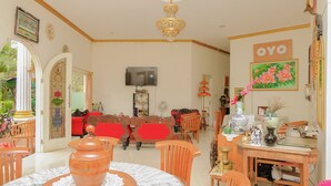 A well-lit living room with a television, a chandelier, and a dining area with wooden furniture. - OYO Life 414 Loji Rejo Guest House (Malang)