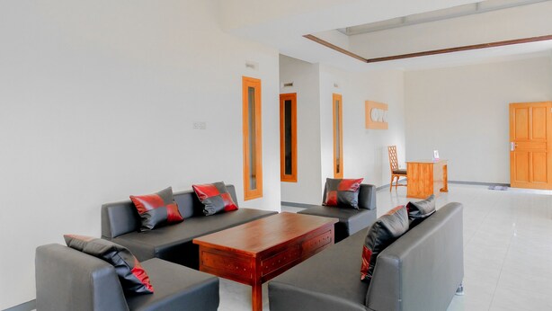 A modern living room with grey sofas and a wooden coffee table, a wooden cabinet, and a small wooden table with a chair. - Hotel O Queen Homestay (Batu)