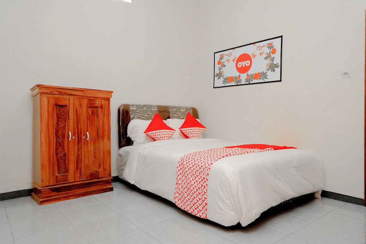 A bedroom with a wooden wardrobe, a bed with red and white bedding, and a framed picture on the wall.