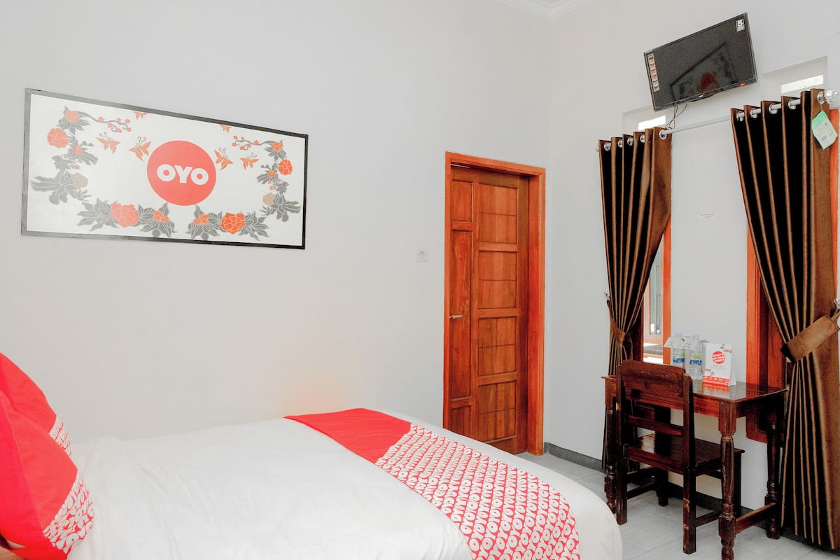 A hotel room with a bed, a wooden door, a desk with a chair, and a TV mounted on the wall.