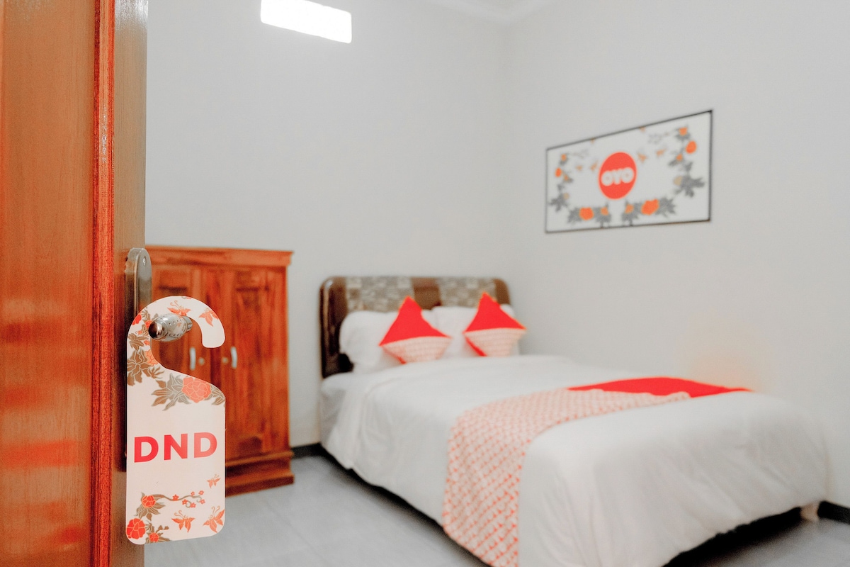 A bedroom with a bed, a wooden wardrobe, a door with a DND sign, and a wall with a circular logo.
