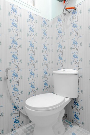 Une salle de bain équipée de toilettes, d’une douche et de murs carrelés ornés d’un motif floral.