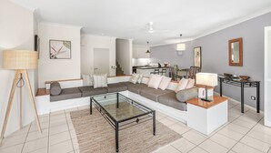 A modern living room with a sectional sofa, a glass coffee table, and a dining area in the background. - Poolside Apt In Alamanda Beachfront Resort 55 (Palm Cove)