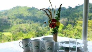A table with a vase of flowers and a plate, set against a view of a lush green landscape. - Mount K Resort - Hostel (Kahawatta)