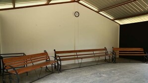 A covered outdoor seating area with three wooden benches and a clock on the wall. - Mount K Resort - Hostel (Kahawatta)