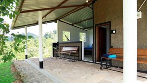 A covered outdoor area with stone flooring, benches, and a view of greenery. - Mount K Resort - Hostel (Kahawatta)