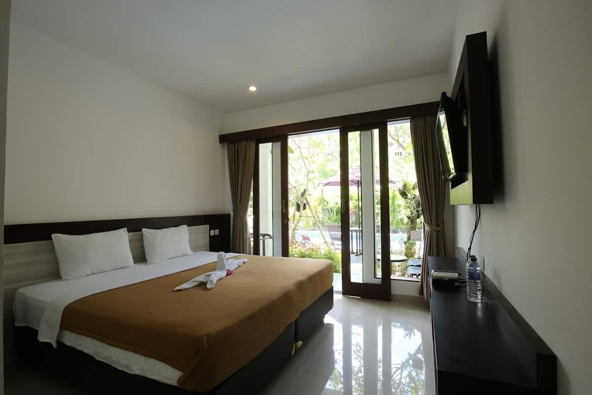 A hotel room with a bed, a TV, a desk, and a sliding glass door to a pool area.