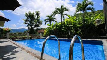 A swimming pool with metal ladders, surrounded by lush greenery and palm trees.