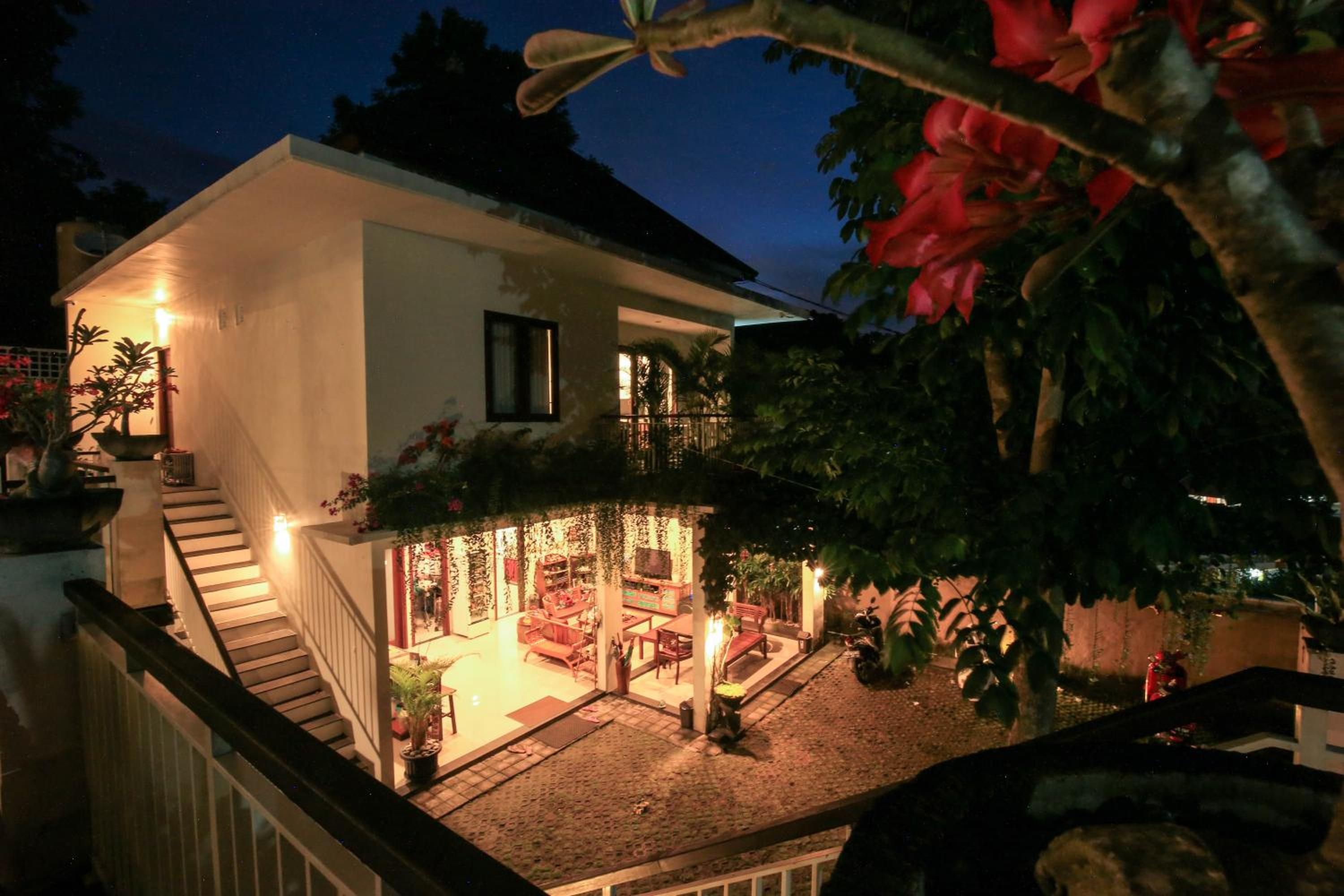 Une maison à deux étages avec un escalier menant à l’étage supérieur, un patio couvert aménagé avec du mobilier et un jardin agrémenté de plantes en pot.