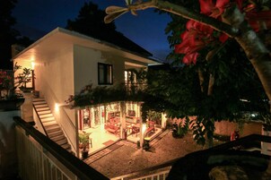 Una casa de dos pisos con una escalera que lleva al nivel superior, un patio cubierto con mobiliario y un jardín con plantas en macetas.